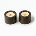 Two lit candles in bronze holders on a white background